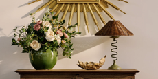 A credenza with a vase of flowers, a leaf-shaped bowl, and a table lamp with a wiggly base