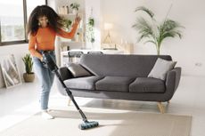 Smiling young woman with vacuum cleaner dancing in living room at home