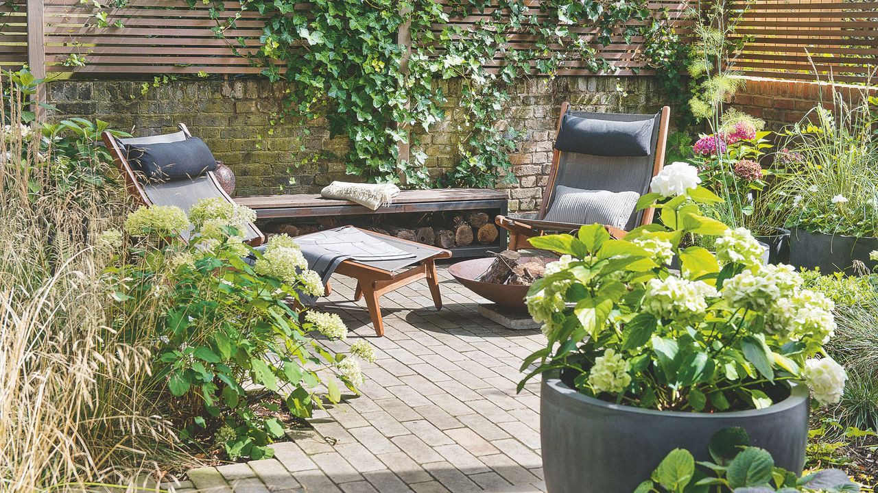 Wooden garden furniture and potted hydrangea plants on block paving patio area in garden