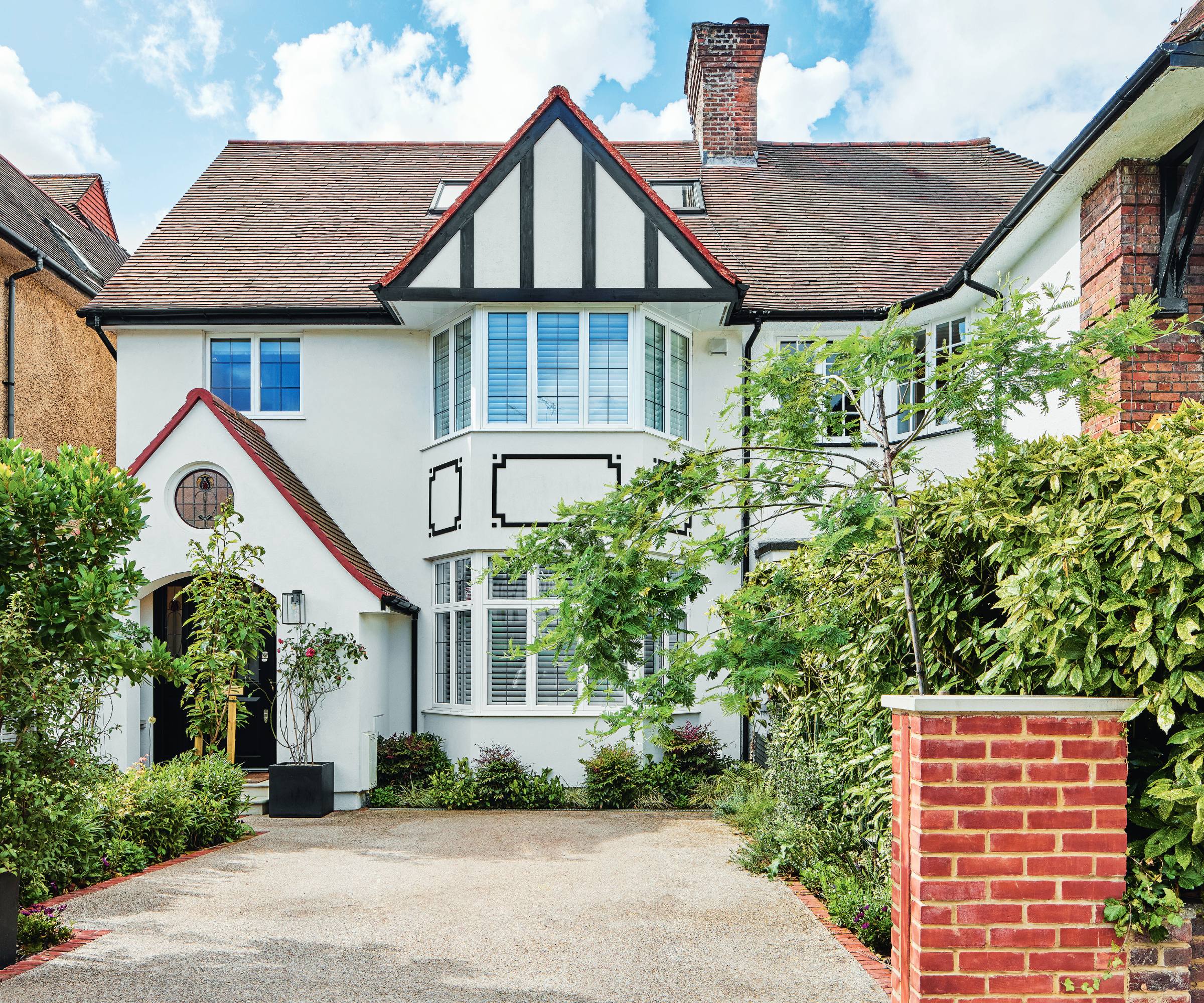 Front elevation of white family semi-detached family house in London with foliage-lined driveway