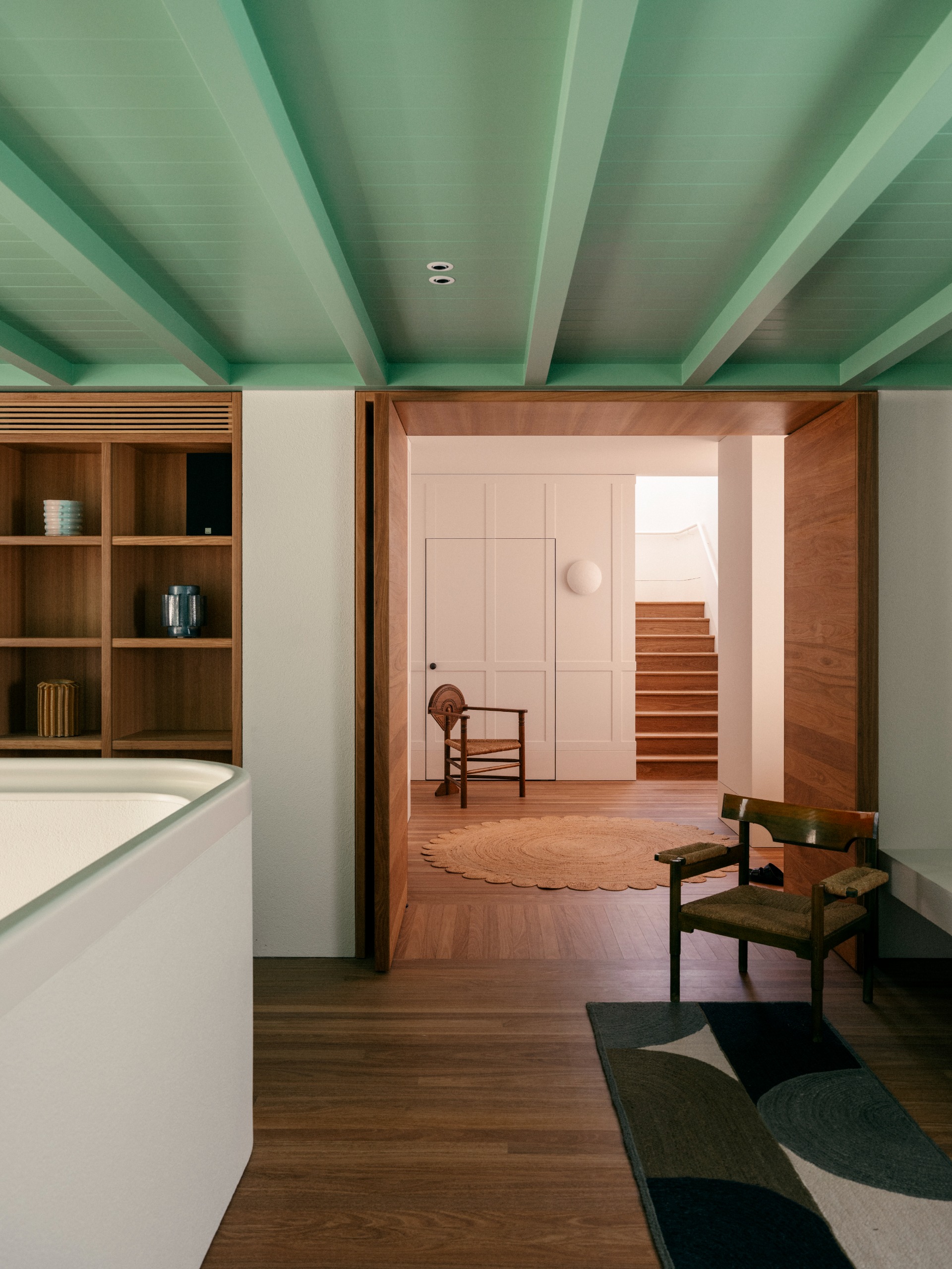 landing in a home with timber built-in bookcase, runner, armchair, and painted mint green ceiling with exposed beams