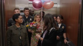 Kelly Clarkson holding baloons and flowers while standing in an elevator and surrounded by The Rookie cast.