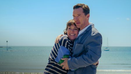 Olivia Colman and Benedict Cumberbatch embrace each other while standing on a beach.