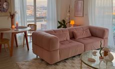 Pink velvet couch in airy living room with wooden floors and round glass-top coffee table
