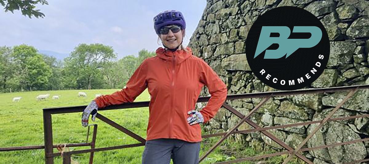 Woman in waterproof jacket by gate with field of sheep behind