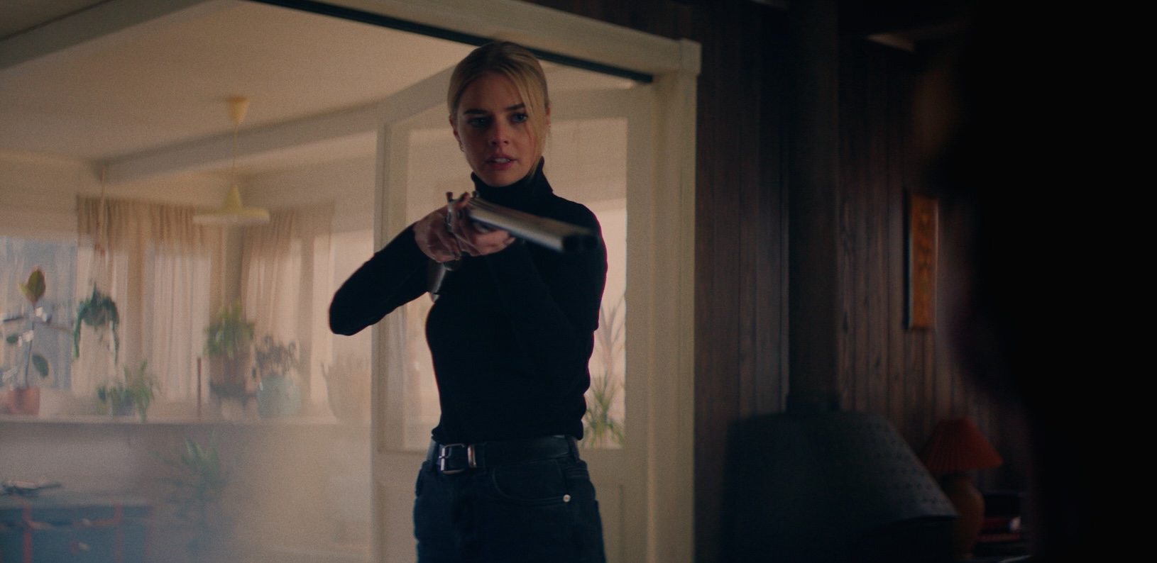 samara weaving pointing a shot gun wearing all black in a dark house in a still from the 2026 thriller over your dead body