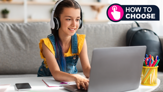 Portrait of little girl in wireless headset using laptop, studying online at home