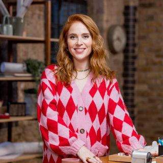 Woman with red hair wearing pink patterned cardigan smiling