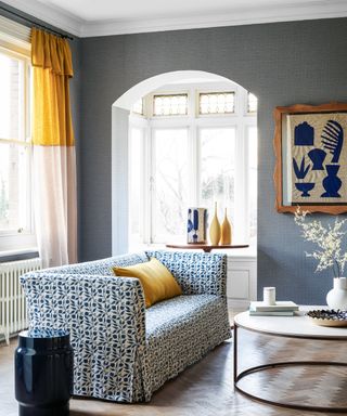 A living room curtain idea with blue patterned wallpaper and yellow and white color-blocked curtain