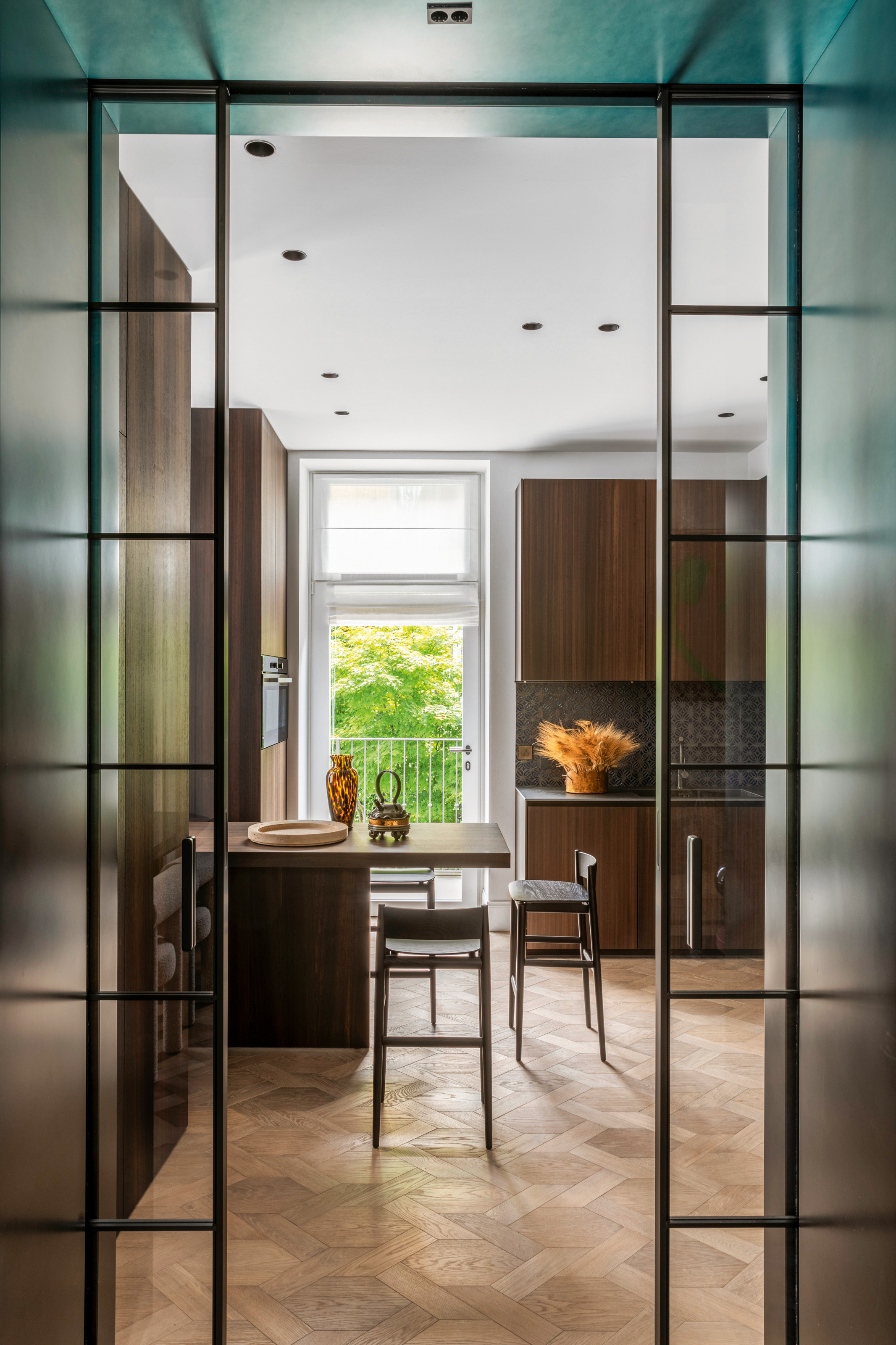View into kitchen with dark wood cabinetry, island overhang with bar stools, and parquet flooring