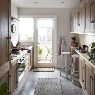 A galley kitchen with slim layout, oak effect shaker cabinets, breakfast bar with stools and large kitchen door to garden
