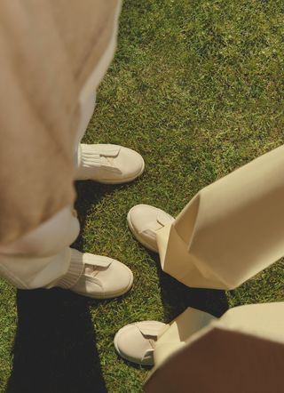 Looking downwards on two people’s feet in white slip-on Zegna sneakers