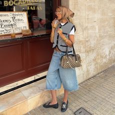 a photo of a woman in front of a coffee shop wearing a vest and jean short outfit that shows the best places to shop for clothes in your 20s