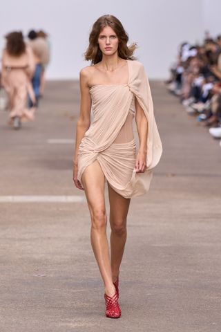 A model at the spring/summer 2025 Stella McCartney show wearing a nude draped minidress with red heels.