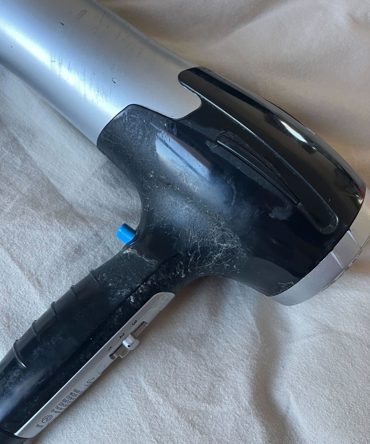 The sticky black handle of a hair dyer laying on cream bedding