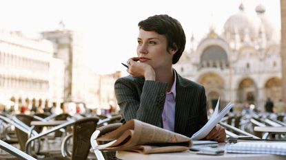 A woman in a business suit sits in a European cafe.