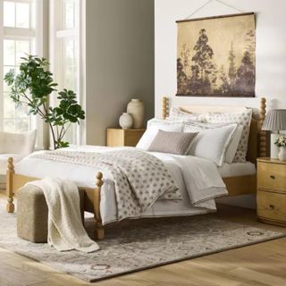 A wooden bedframe with white and gray bedding with a tapestry hanging above