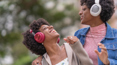 African American twin sisters wearing headphones enjoying music in the park, wearing jackets because of the cold.