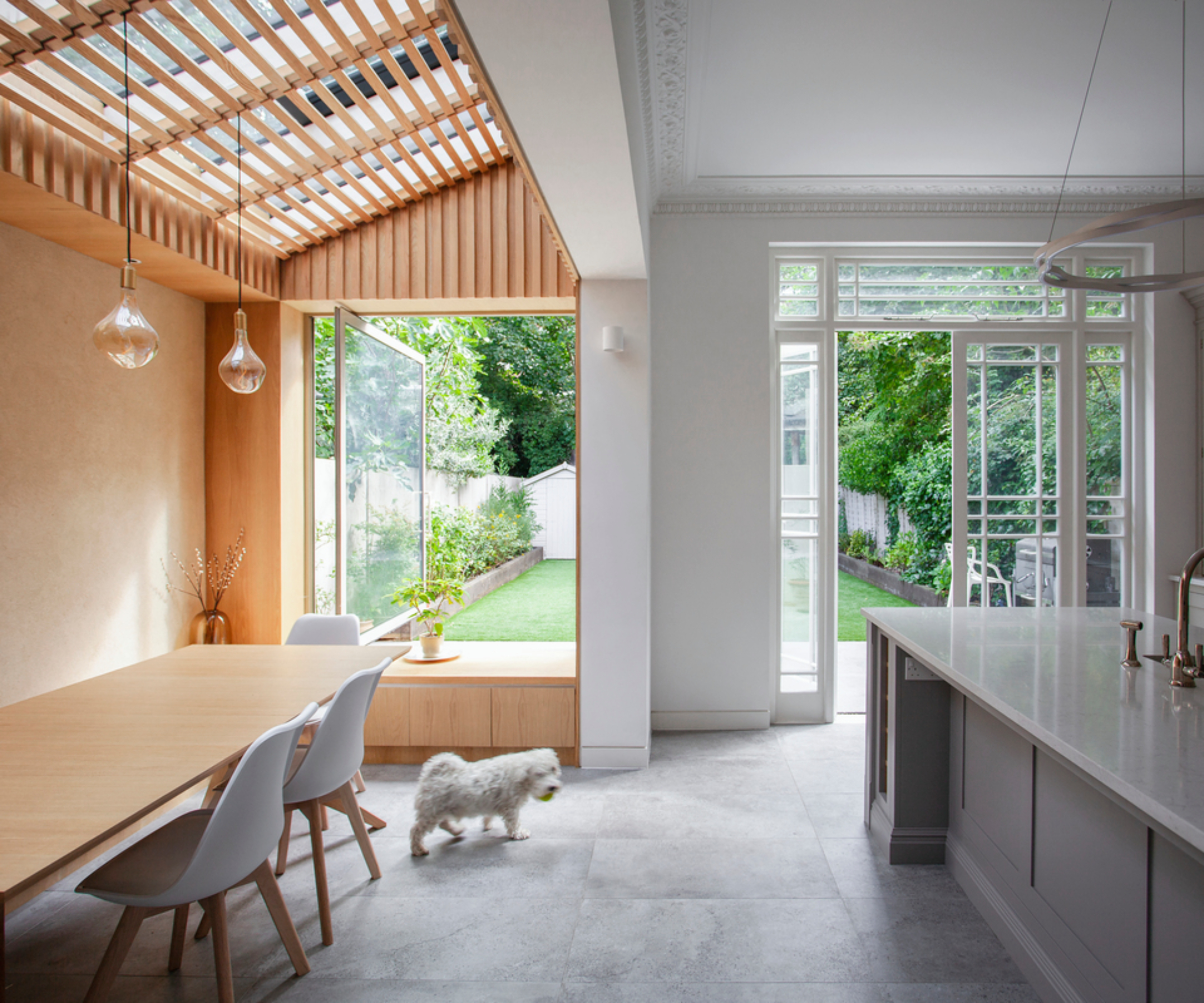 inside side extension with slatted wooden design below glass roof, large picture window at one end with wooden window seat, dining area and kitchen