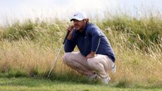 Brooks Koepka crouches down in the grass at Royal Hoylake in 2023