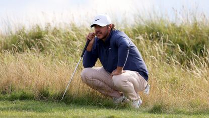 Brooks Koepka crouches down in the grass at Royal Hoylake in 2023