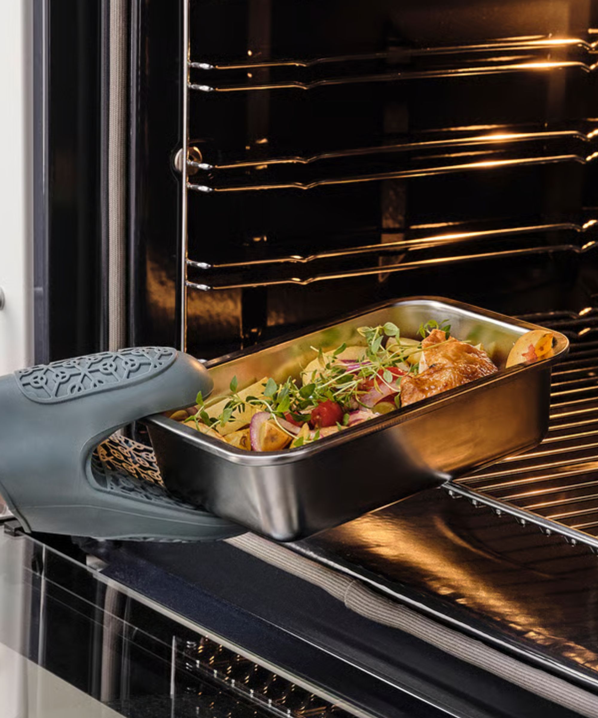 A small rectangular stainless steel food container being removed from an oven with a silicone glove
