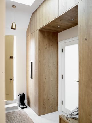 hallway/entryway with wooden built in storage, white flooring, rug, pendant light, white walls
