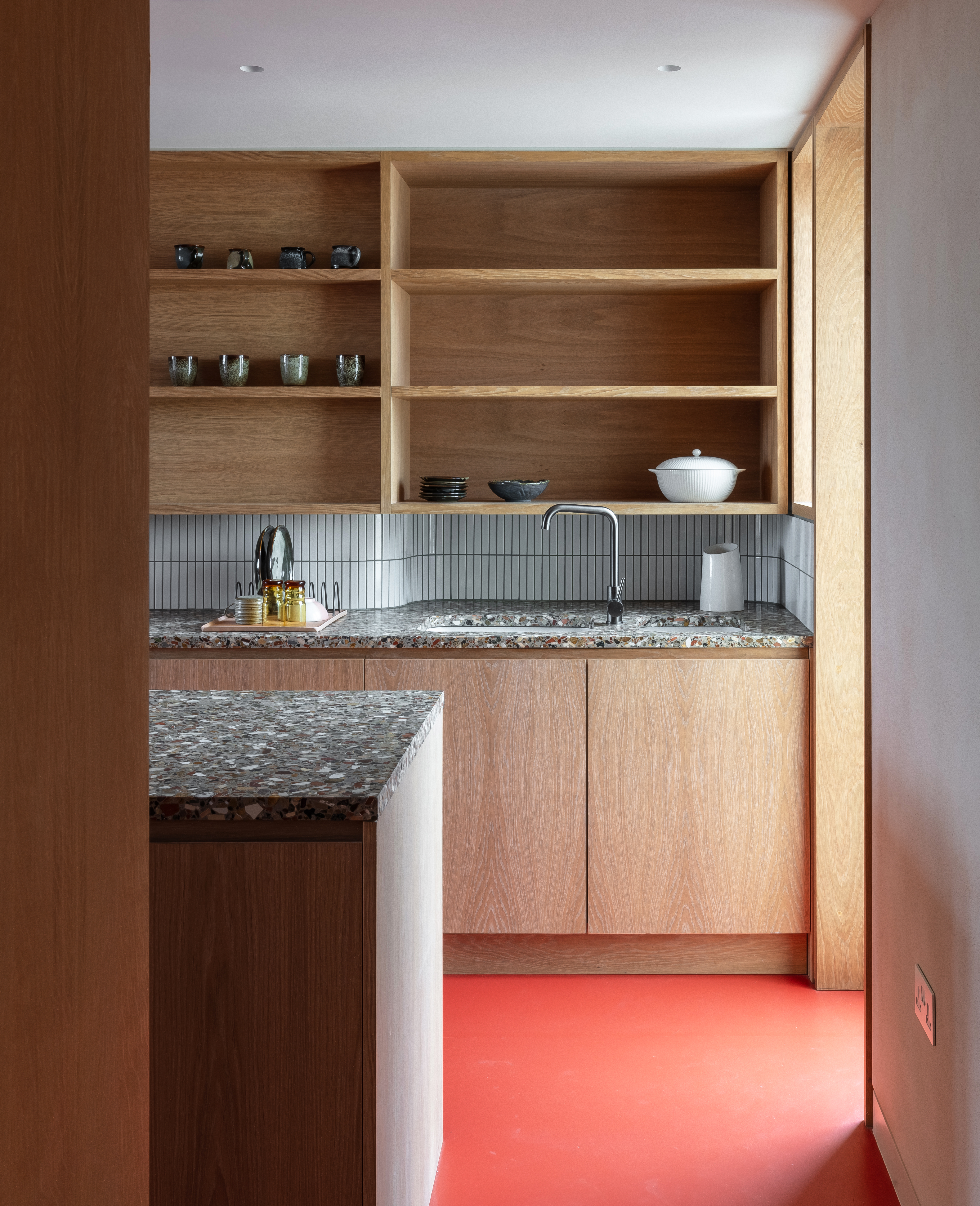 A kitchen with red pigmented flooring, and wooden open cabinets