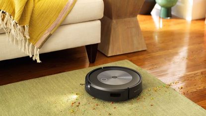 iRobot Roomba Cyber Monday deals. iRobot vacuum hoovering rug on wooden floor, sofa in background with yellow throw