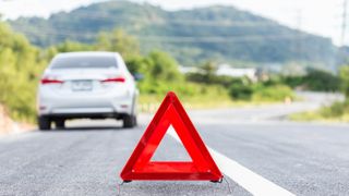A warning triangle positioned behind a broken down car on the road