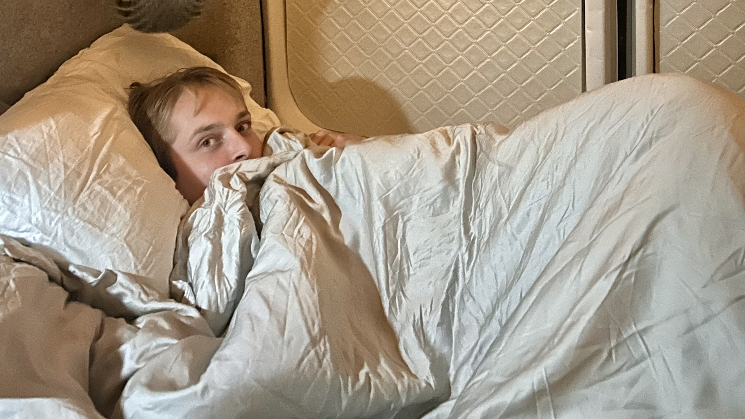 A man in bed with a duvet up around his chin