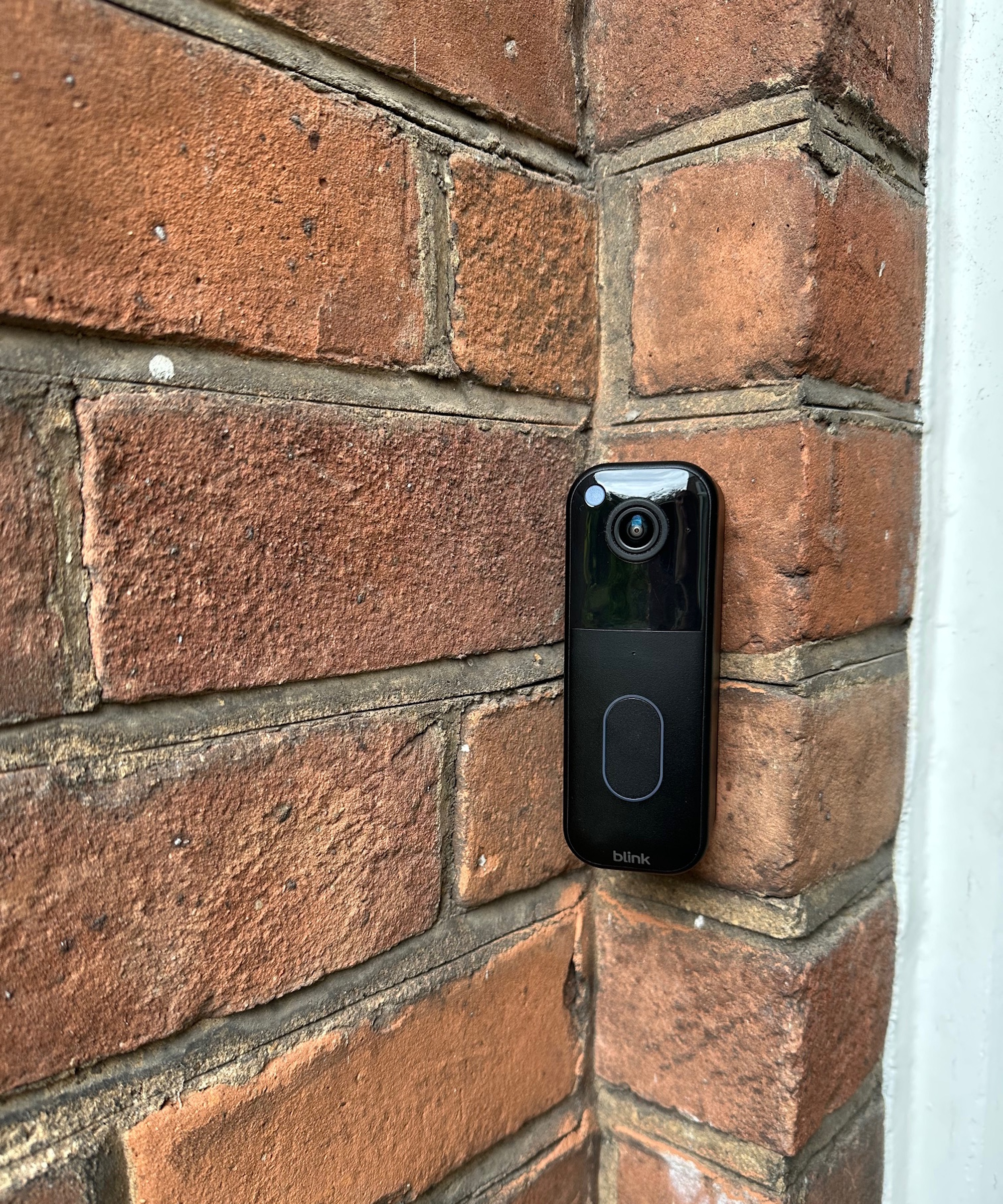 Black Blink video doorbell attached to outside brick wall.