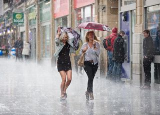 Two women running down a street in a rainstorm.