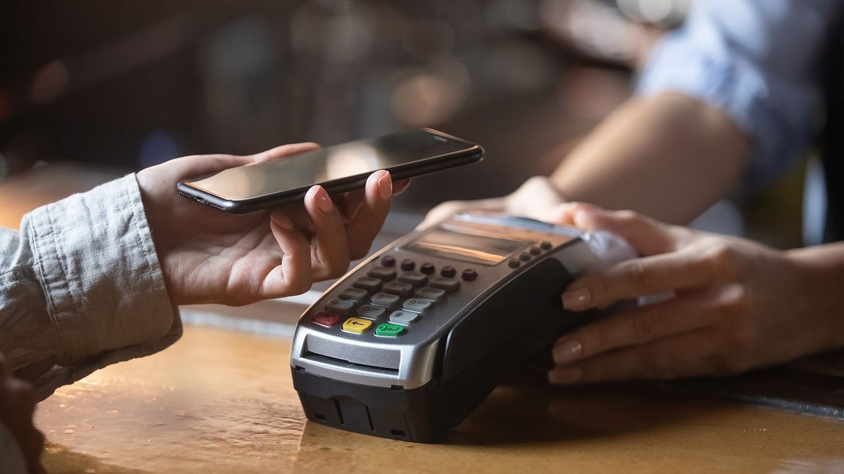 A person holding their smartphone over a payment terminal to make a contactless payment