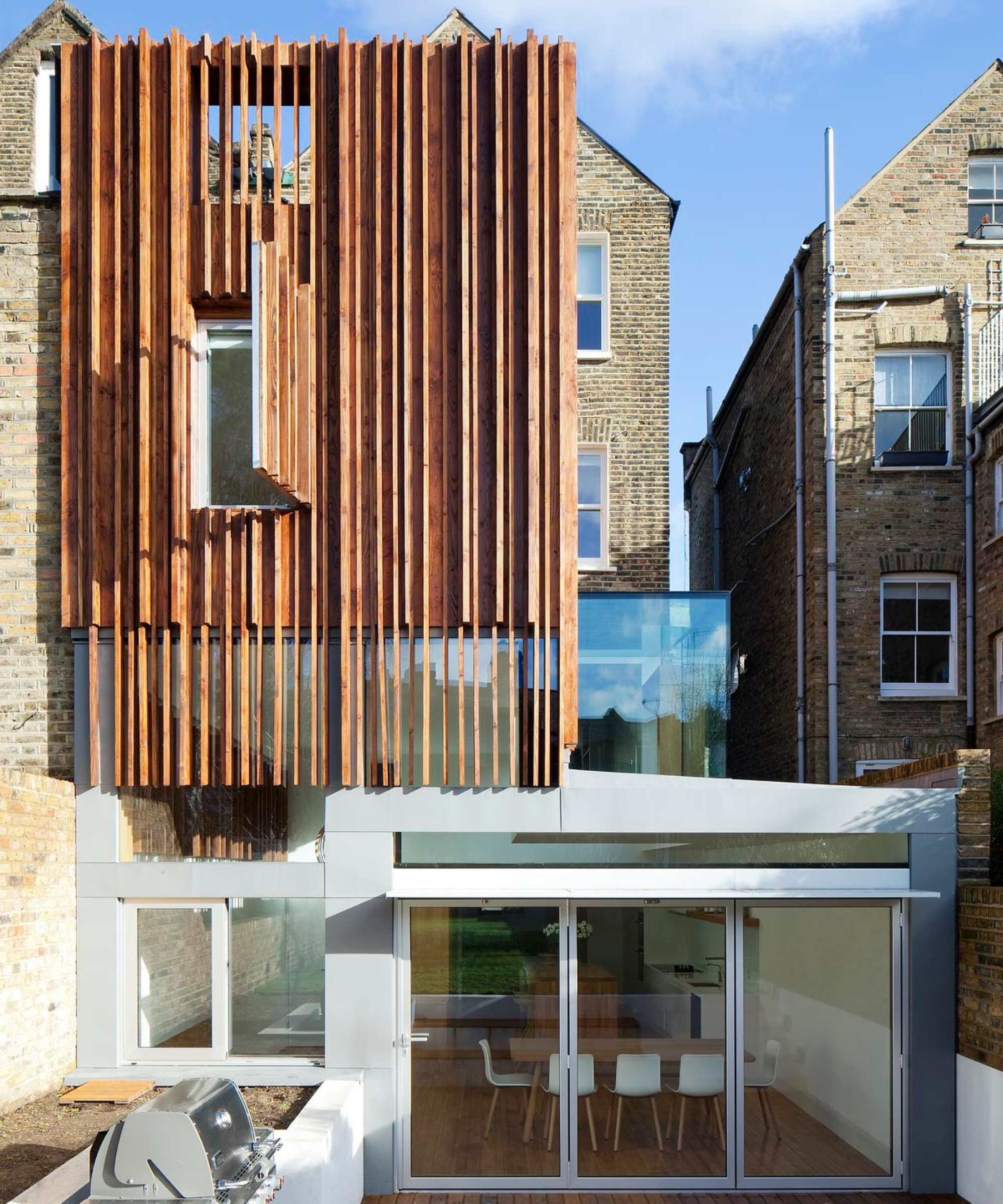 double storey extension featuring large strips of timber reaching up from glass and render extension with part glass box roof