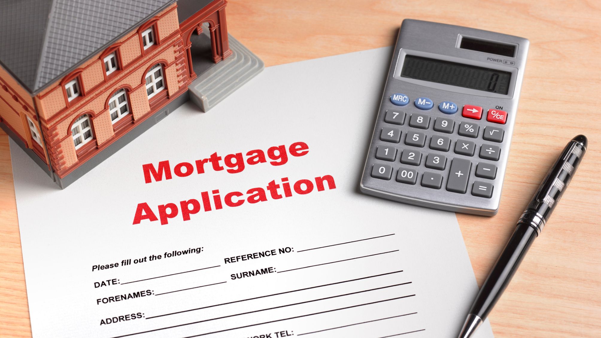 A mortgage application on a desk next to a calculator and tiny model home.