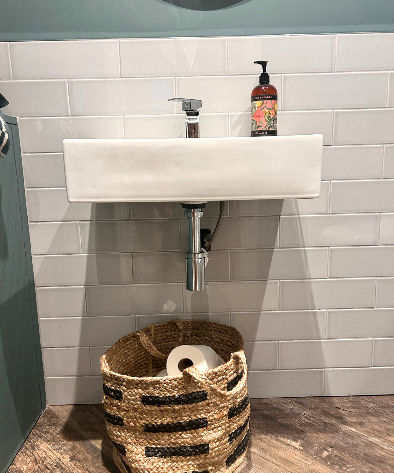 Gray and green bathroom with basket full of toilet rolls and white sink