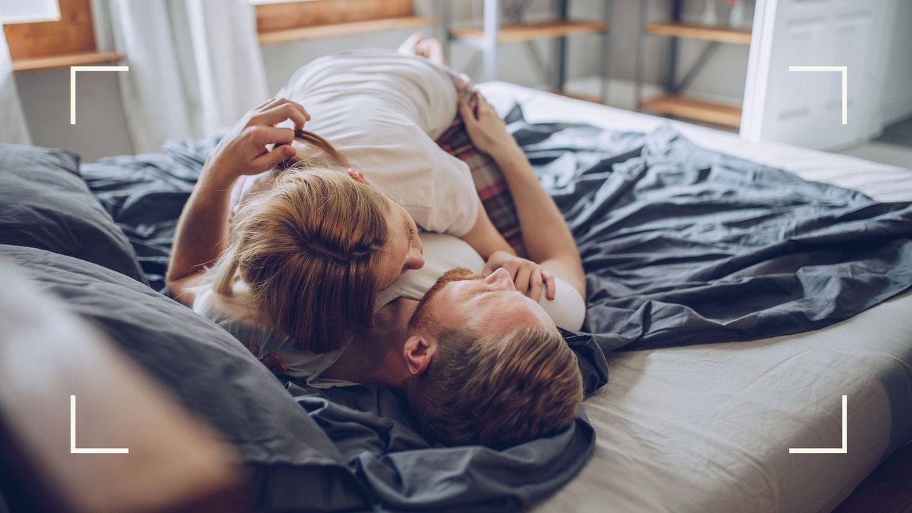 Woman lying on top on man on bed in sunlit bedroom, to represent the reverse cowgirl sex position