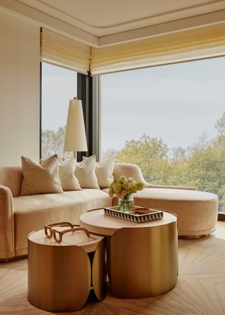 Beige rounded chaise sofa in a neutral hotel living room and a gold nesting coffee table