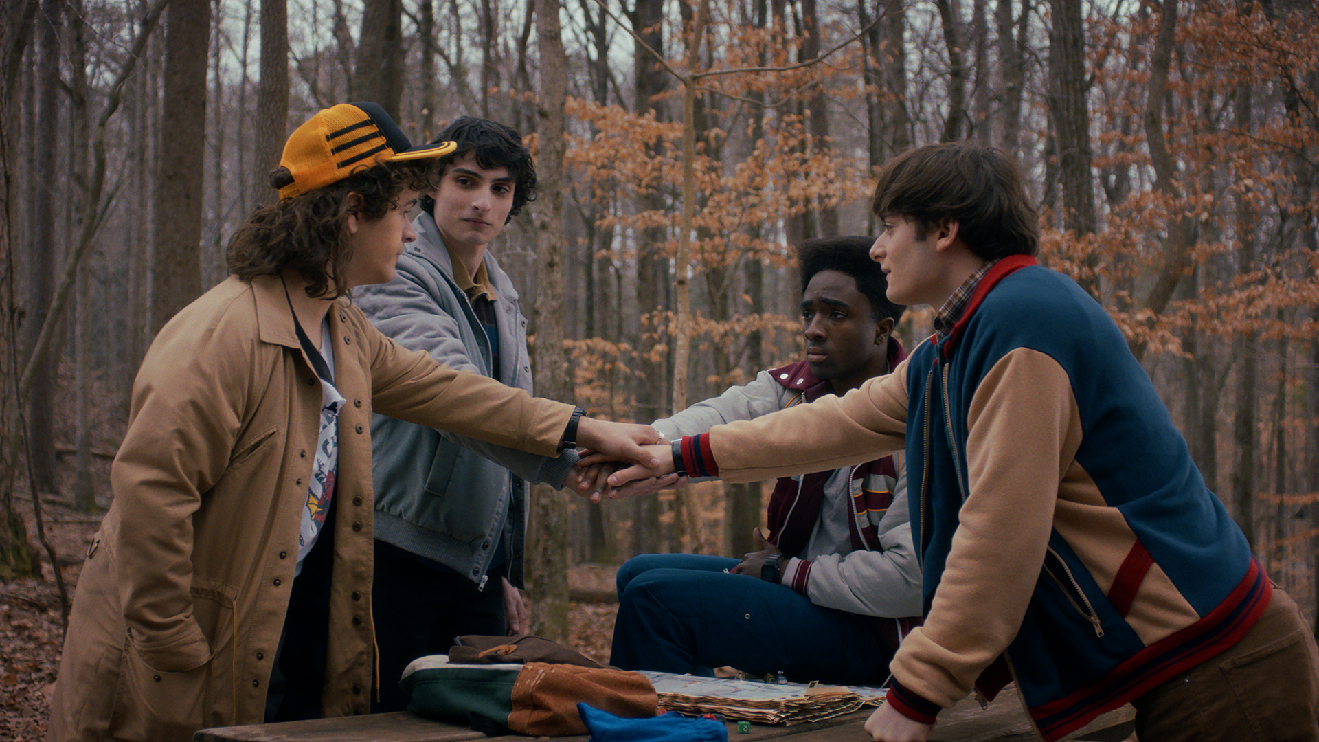 Dustin, Mike, Lucas, and Will putting their hands out and on top of each other's in Stranger Things season 5