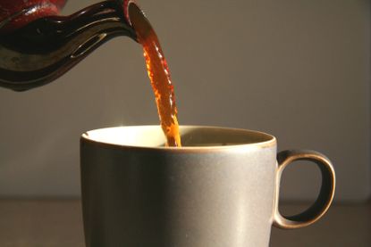 Tea being poured from a brown teapot into a mug