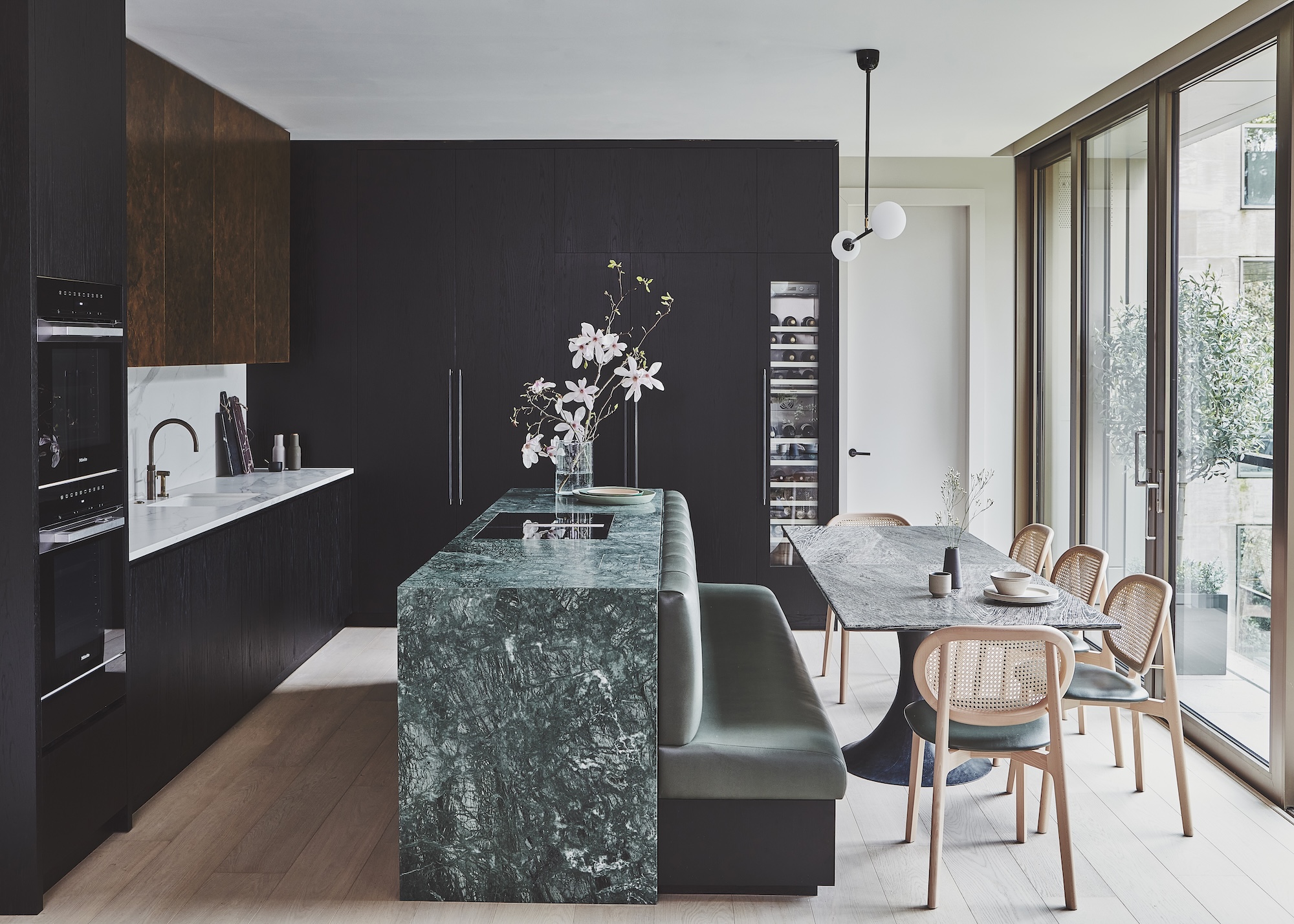 a modern kitchen with a mix of handle-less cabinets with handles on the tall units and appliances. Also with an island that has a built-in bench seat