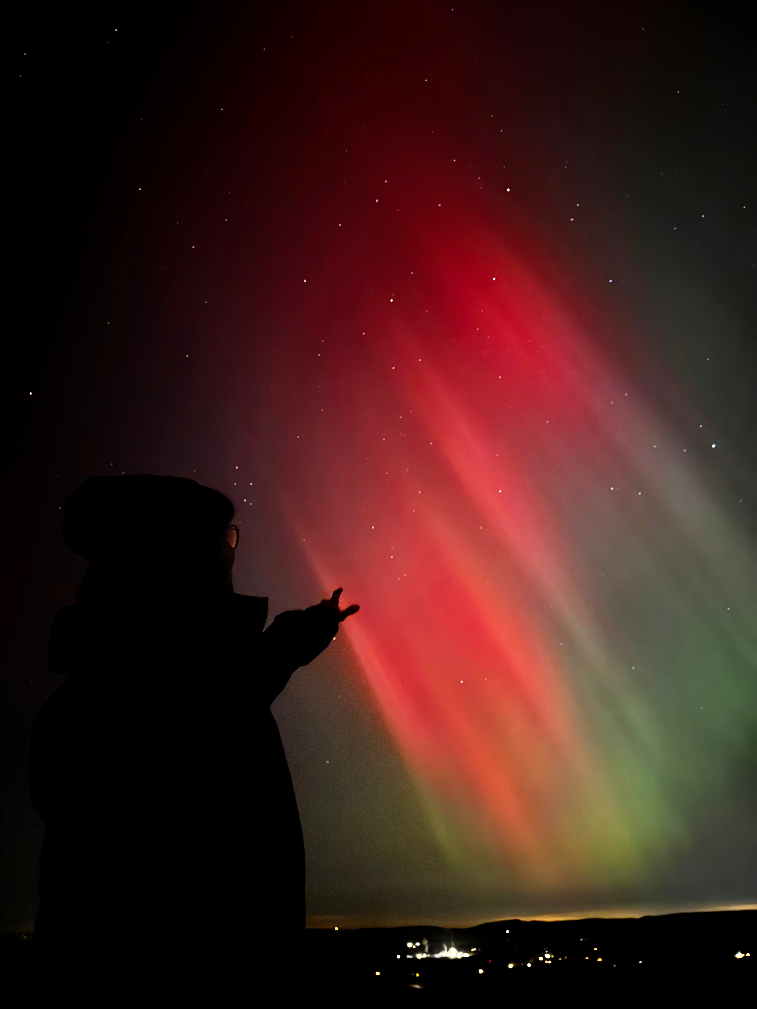 A person pointing at the Northern Lights in the night sky