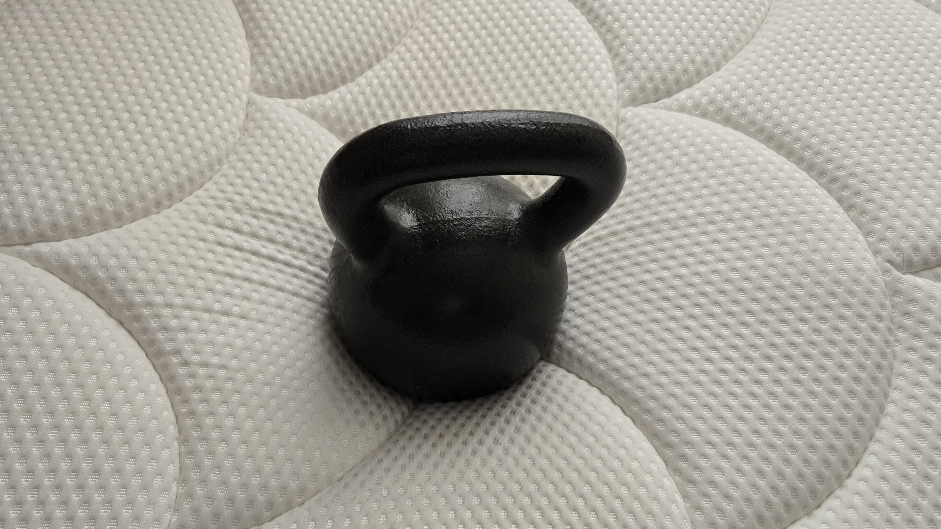A small black dumbbell resting on the surface of the DreamCloud mattress