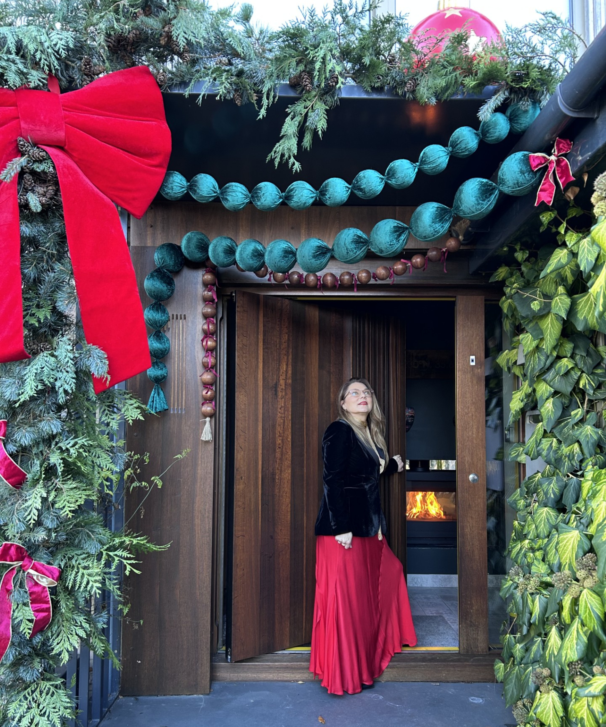 female stood outside large front door decorated with a seasonal doorscape featuring a large bows, garlands and baubles