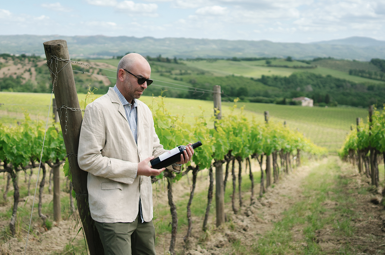 Man looking at a bottle of wine in a vineyard