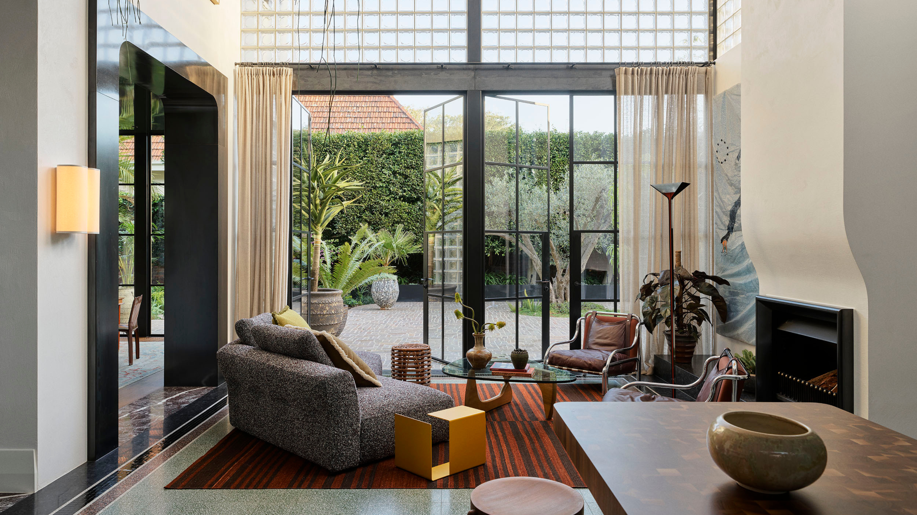 a contemporary living room with a sculptural fireplace and steel glass french doors