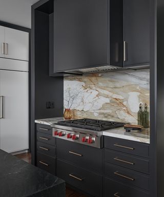 A kitchen with dark cabinetry and marble backsplash
