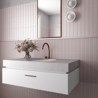 A pale pink bathroom featuring fluted pink tiles and a white stone basin