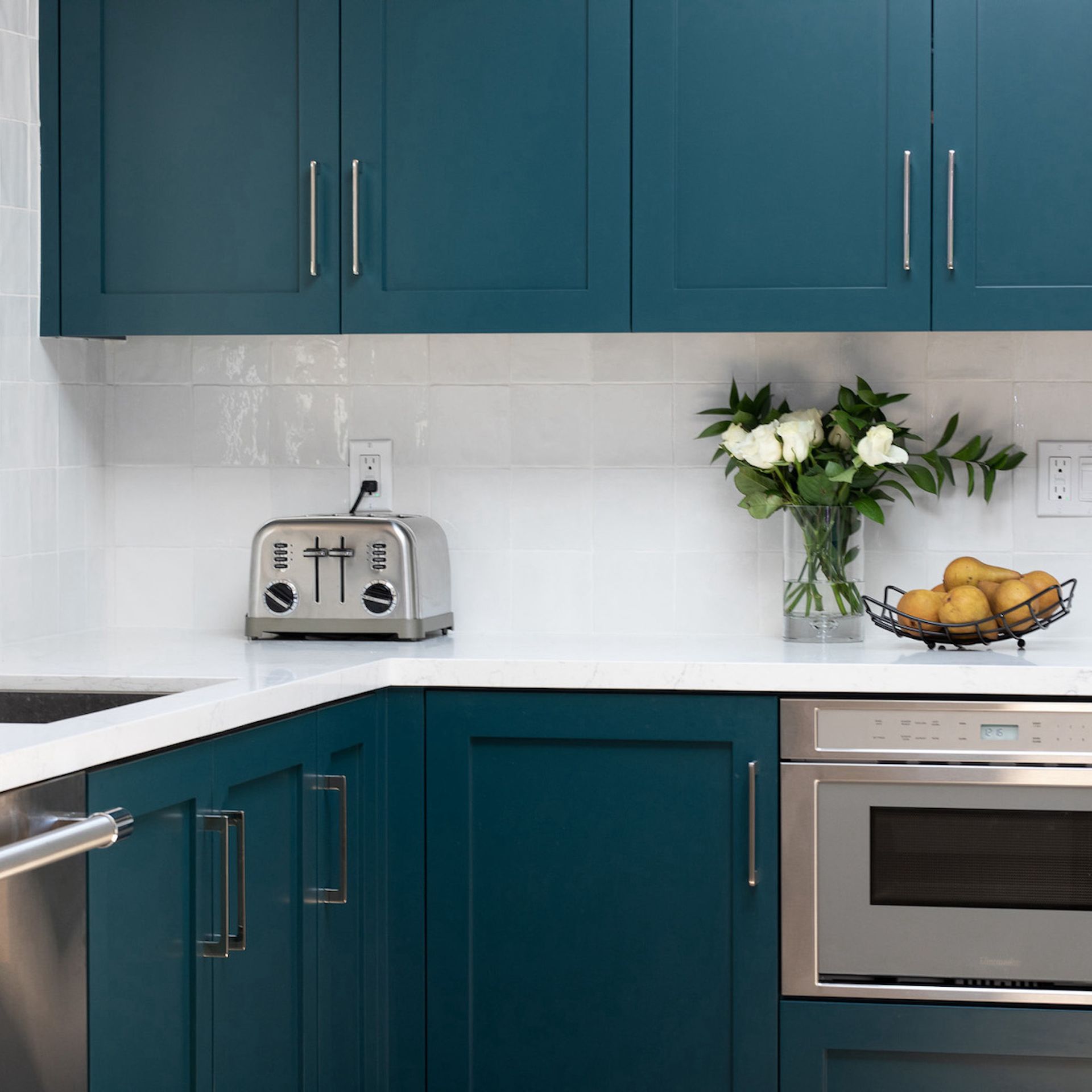 Area dapur dengan kabinet teal, countertop putih, dan backsplash